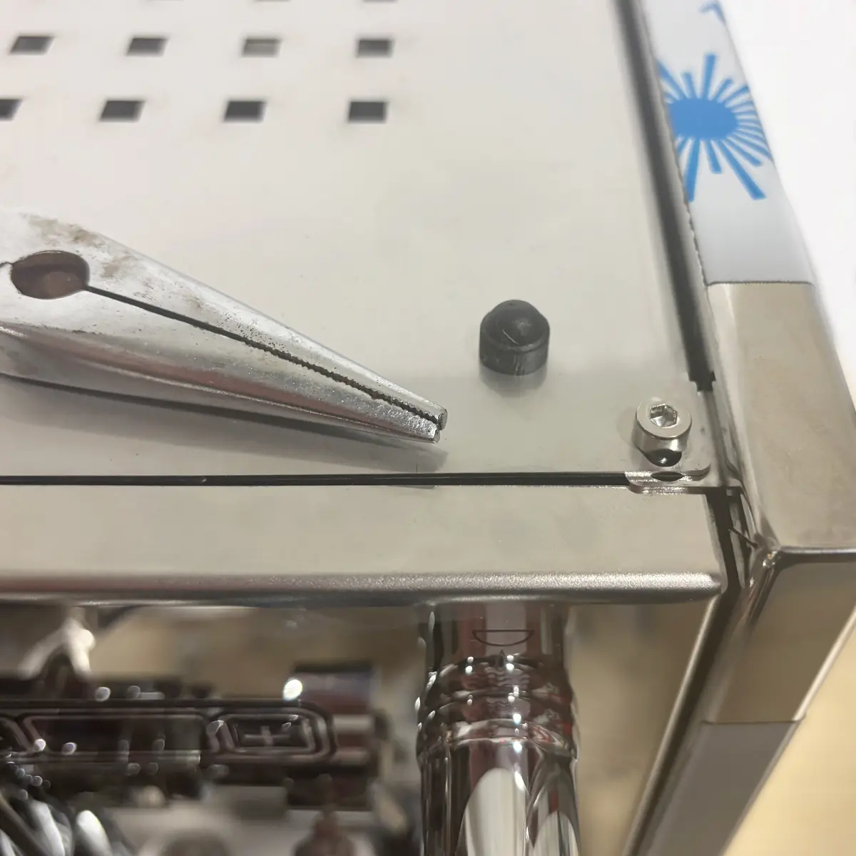 Pliers removing plastic cap from top panel screw of Bezzera Sole espresso machine, revealing access to internal components for maintenance.