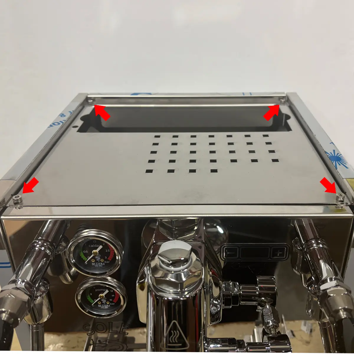 Top panel of Bezzera Sole espresso machine showing four Allen-head screws at corners, with visible pressure gauges and steam valves below, indicating access for maintenance.