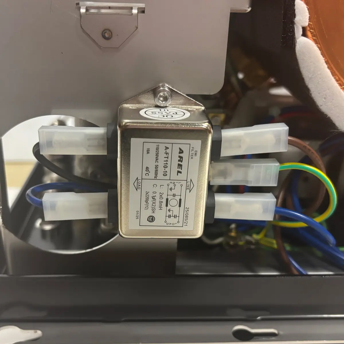 Close-up of an electrical component labeled &ldquo;AREE AF1T51110C&rdquo; with wires connected to its terminals, inside a machine with visible colored wiring in the background.