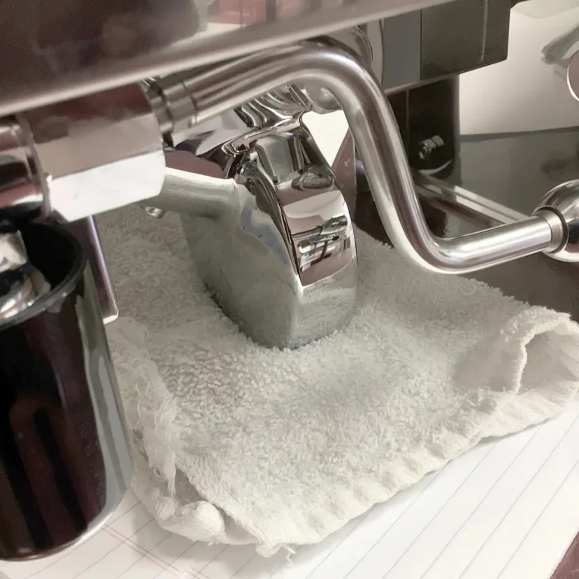 A close-up of a Magister Stella coffee machine’s metal group head resting on a folded white towel, with part of a black portafilter and a handwritten notebook visible underneath.