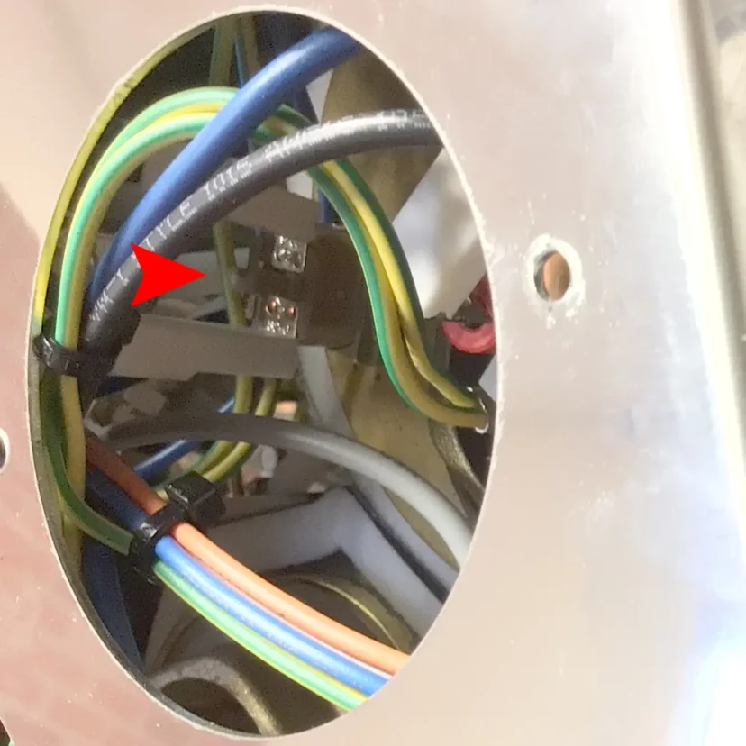 A close-up view of electrical wiring inside a metal socket box, with various colored wires and a red arrow pointing to a black wire labeled Magister Stella—not steam or hot water.
