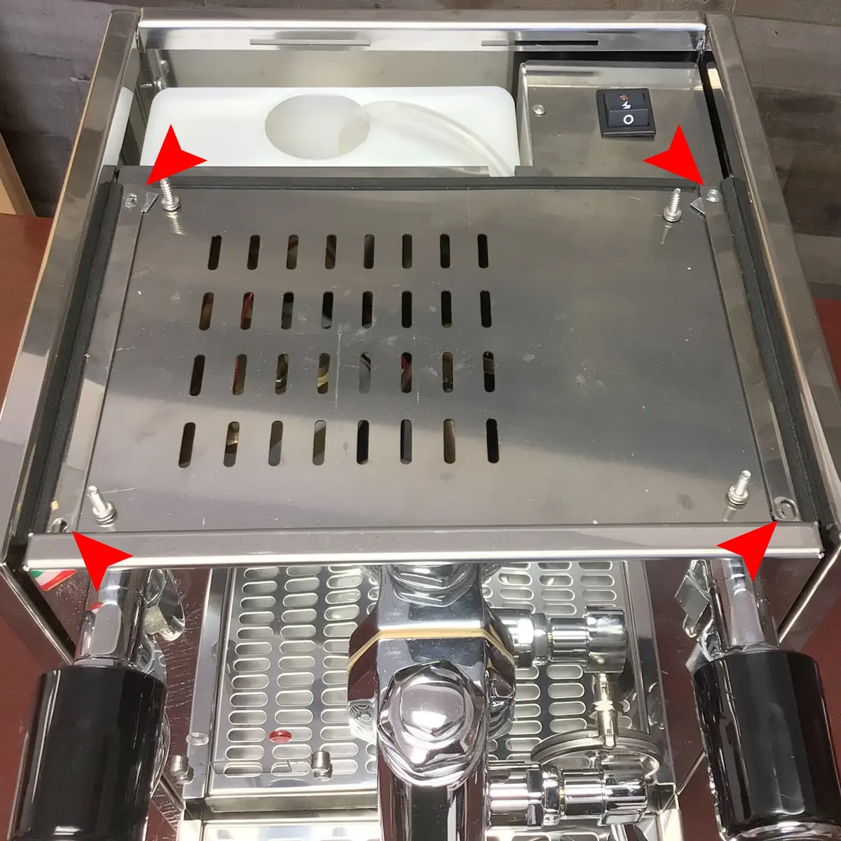 A Magister Stella stainless steel espresso machine with its top panel held by four screws, each marked with a red arrow, shows the water tank underneath—perfect for those interested in accessing the inside for maintenance or inspection.