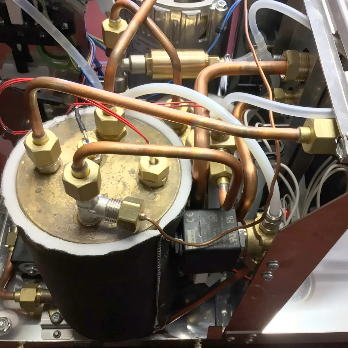 Close-up view inside a Magister Stella coffee machine, revealing copper pipes, brass fittings, wires, and tubes all connected to a cylindrical metal boiler.
