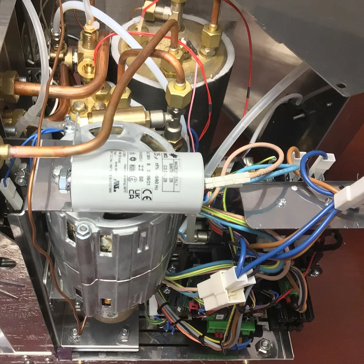 Close-up view of the internal components of a Magister Stella espresso machine, showing wiring, copper pipes, and metal parts—Accessing the Inside highlights the complexity of its electrical and hydraulic systems.