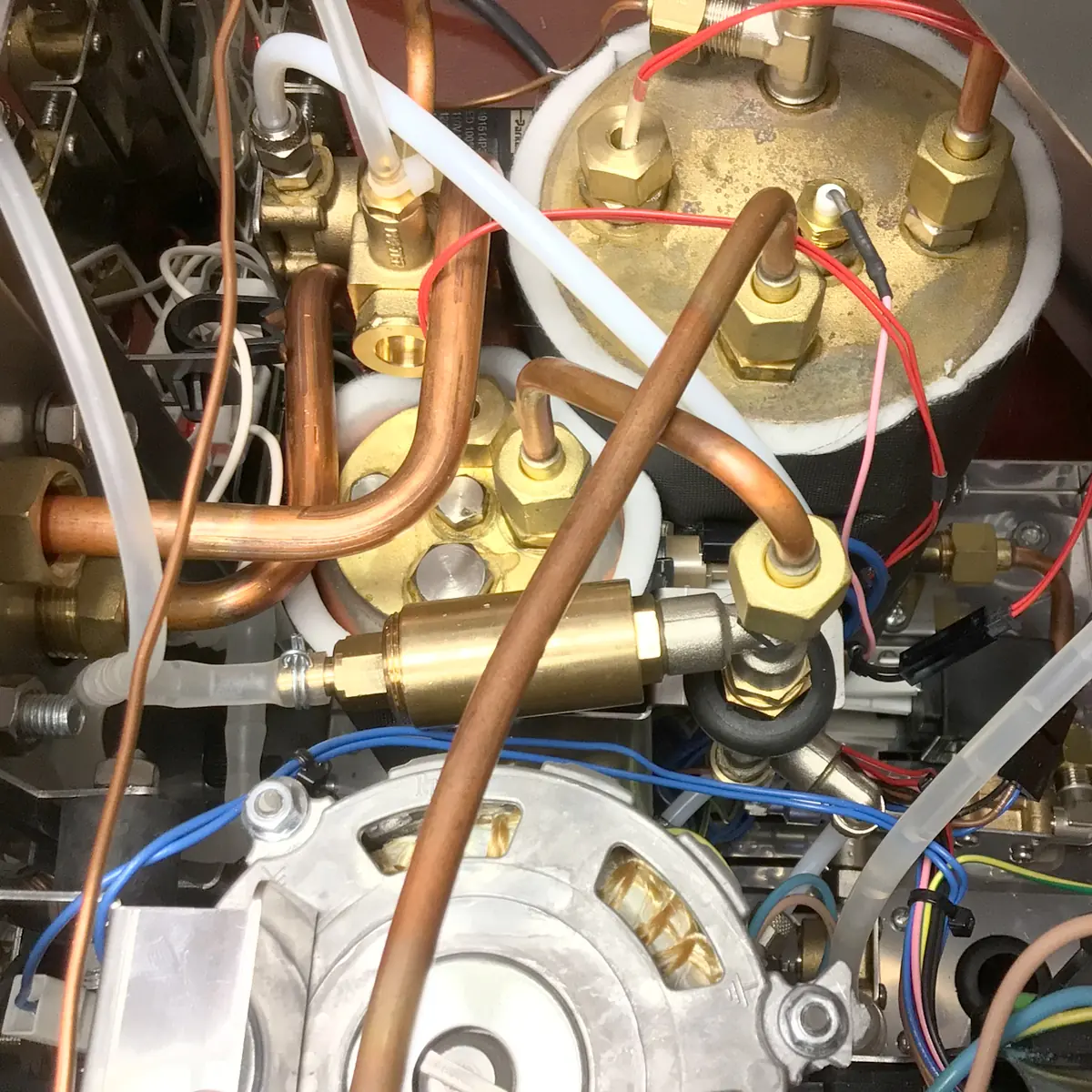Close-up view inside a Magister Stella espresso machine, highlighting internal mechanical and electrical components—metal pipes, brass fittings, wires, and connectors all arranged in a compact space.