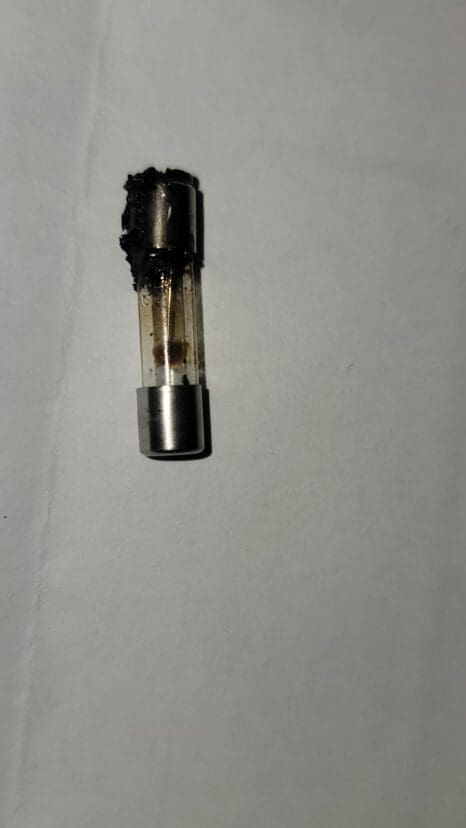 A burnt vape cartridge with a damaged, blackened top and some residue inside, lying on a white surface.